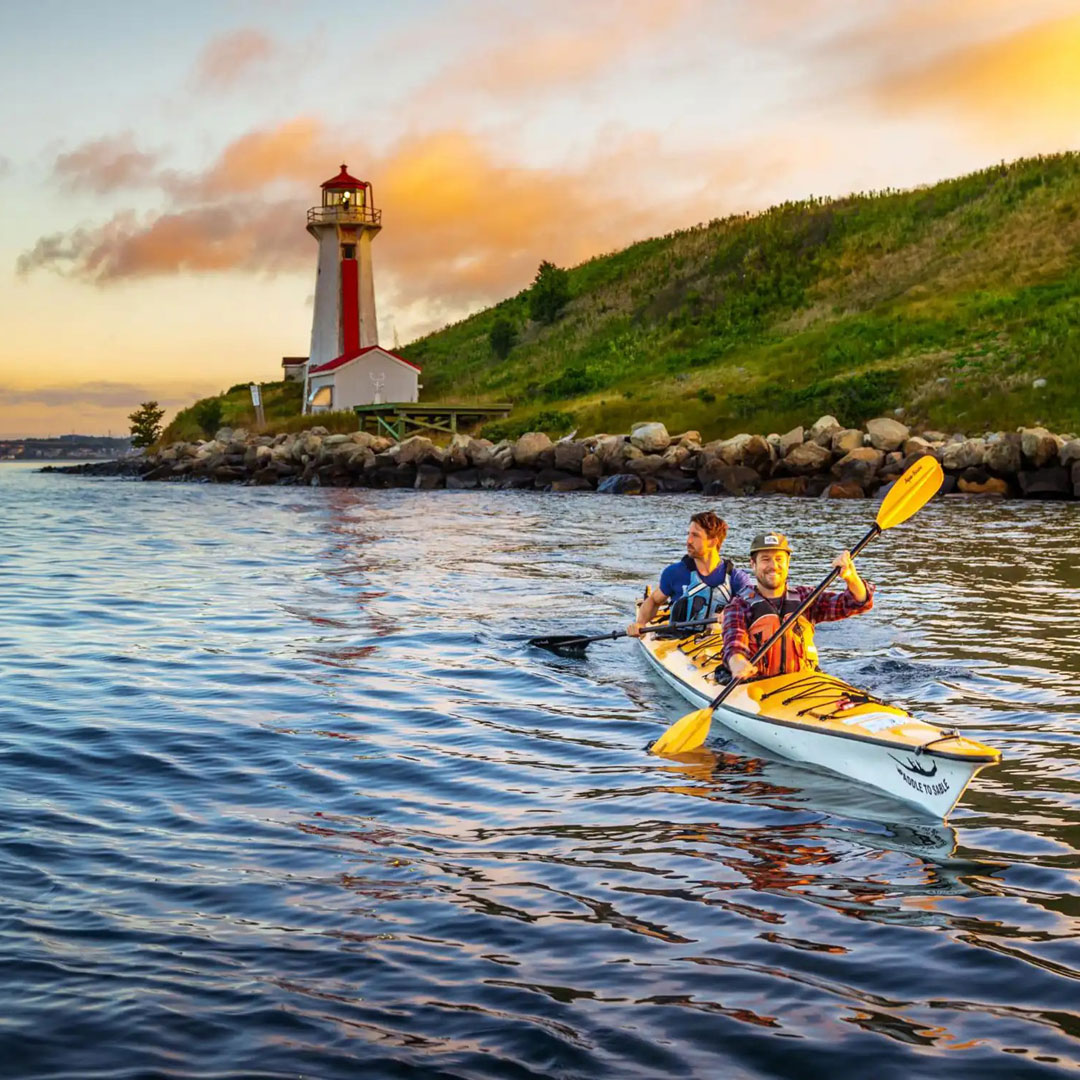 Two kayakers paddling near a lighthouse.
